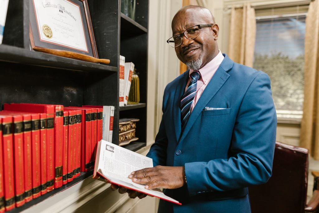 Professional lawyer in formal attire holding a book, smiling in an office setting surrounded by law books.